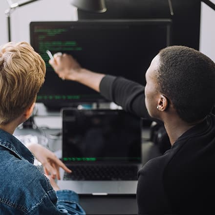 An instructor looking at code on a computer with a student who wants to get into tech.