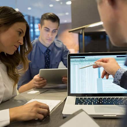 Three accountants pouring over data on a laptop screen.