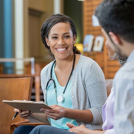 A certified health education specialist holding a clipboard and speaking with a community member.