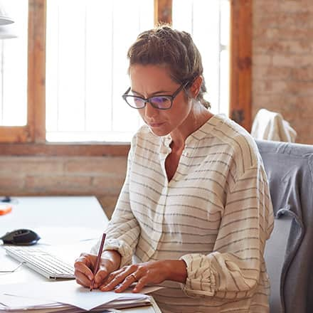 A copywriter writing in a notebook at her desk at a marketing agency.