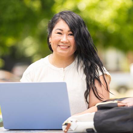A student choosing a college on her laptop while outdoors.