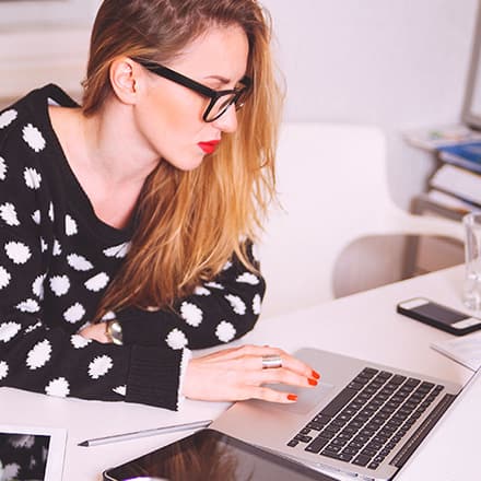 Woman sitting at a desk using a laptop to research how to get a scholarship.