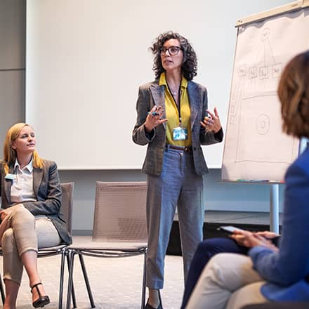 An industrial-organizational psychologists standing at the front of the room presenting to other psychologists. 