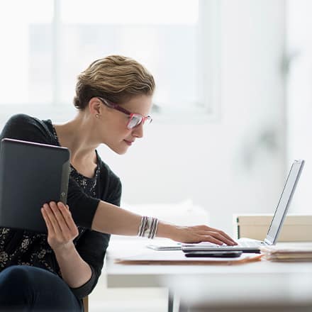 A woman who earned an online MBA holding a tablet and working on a laptop.