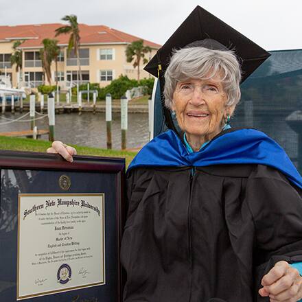 Joan Donovan dressed in graduation cap and gown, holding her SNHU diploma outside of her Florida home.