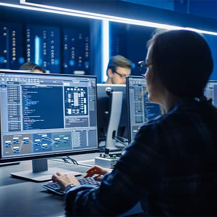 A woman with a ponytail and glasses coding in a computer lab.