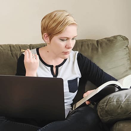 Jolene Stetz studying a textbook with a laptop in front of her.