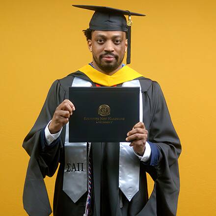 Josiah Lee, a 2025 master's in cybersecurity graduate from SNHU, wearing a cap and gown and holding his diploma.