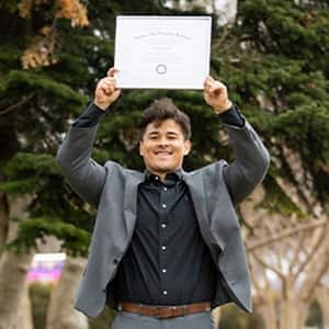Kevin Bucardo '25MBA, MBA with a concentration in Finance graduate from SNHU, holding his diploma over his head.