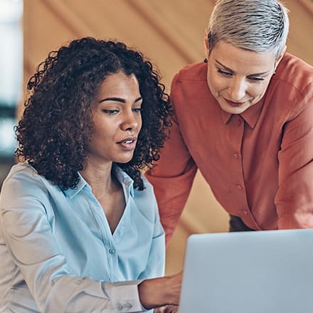 Two management accountants discussing information on one of their a laptops.