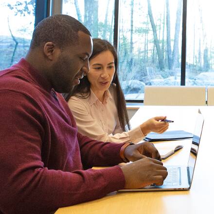 Two business professionals on their laptops at a conference table, discussing MBA vs MS degrees.