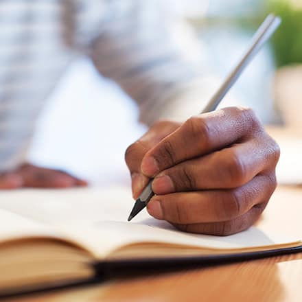 The hand of an MFA student holding a pencil and writing in a notebook