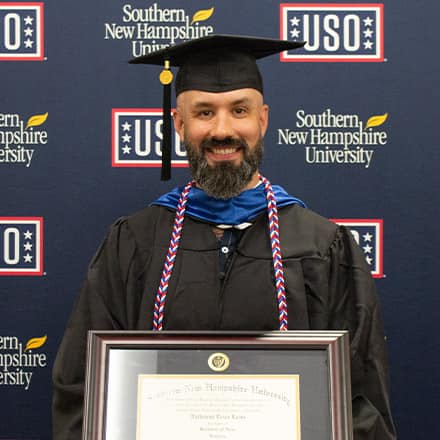 Nathaniel Lohn holding his diploma in front of USO and SNHU sign