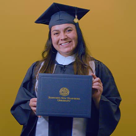 Paola Andrea Gaona Salamanca, a 2026 SNHU graduate who earned her bachelor's in business administration wearing her cap and gown and holding her diploma in front of a yellow background.