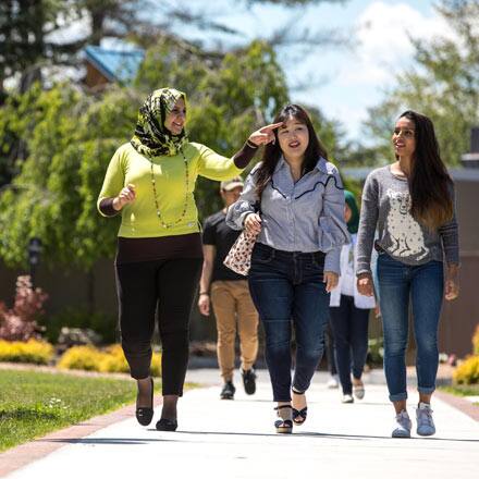 Three women walking down a path on a college campus.