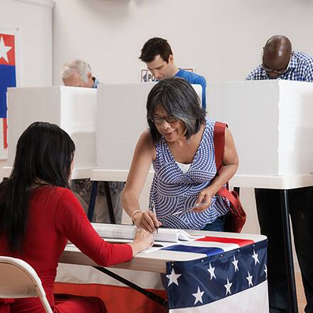 A woman registering to vote with voting booths behind her.
