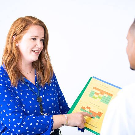 A healthcare professional exhibiting some qualities of a good leader as she points to a chart on her clipboard and listens to a team member.