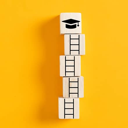 A stack of five building blocks on a yellow backdrop: the bottom four blocks feature pieces of a ladder and the top depicts a graduation cap.