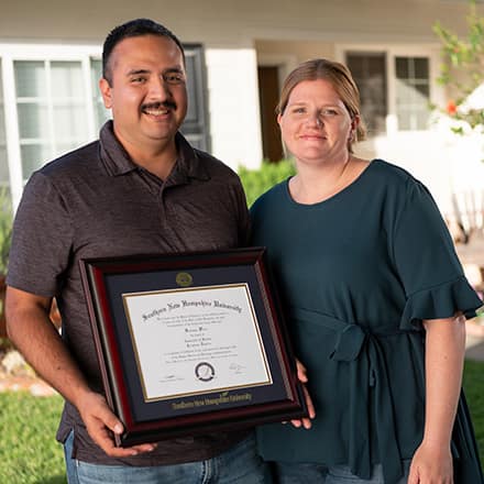 Sal and Shelly Villa in front of their home with Sal holding his framed diploma.