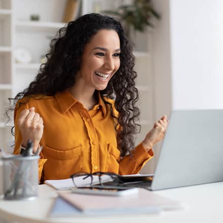 A woman smiling while celebrating a small win at her laptop.