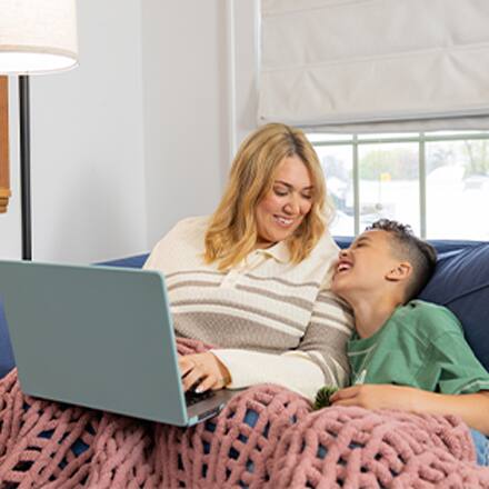 SNHU graduate Madison Richards and her son Malakai sitting on a couch while she works on a laptop, completing her online degree program.