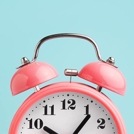 The top half of a pink alarm clock with two bells on top.