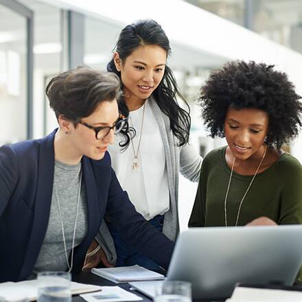 Three business professionals reviewing a presentation on a laptop.