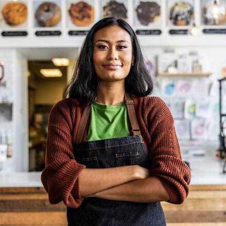 An entrepreneur wearing an apron standing in front of a desk in her business.