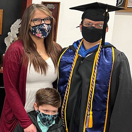 Nicole Staller dressed in graduation cap and gown with wife Bridget and son Brayden.