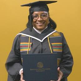 Valerie Craig, a 2025 graduate from SNHU with an associate degree in liberal arts, dressed in a cap and gown and holding her diploma.