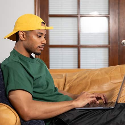 Keyon Tuiteleleapaga, an SNHU graduate with a bachelor's in human services and master's in psychology, using a laptop on his couch.