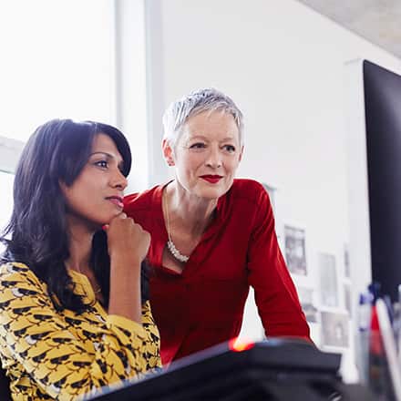 Two women sitting in front of a desktop while considering what you can do with an MBA