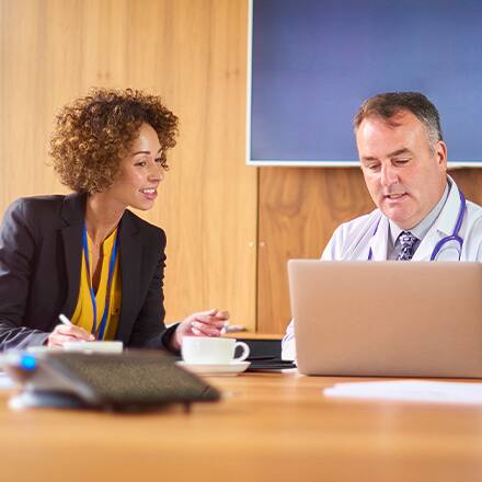 A public health professional discussing a project with a doctor as they both look at a laptop