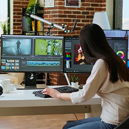 A game developer editing gameplay footage on a multi-monitor workstation.