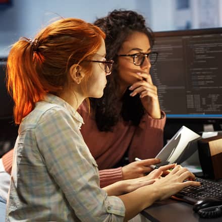 Two software engineers reviewing code on two desktop monitors.