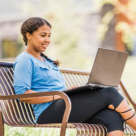 A person sitting on a bench, researching what an undergraduate degree is on a laptop.