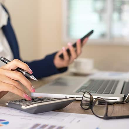 A person sitting at a desk with a laptop and calculator bookkeeping.