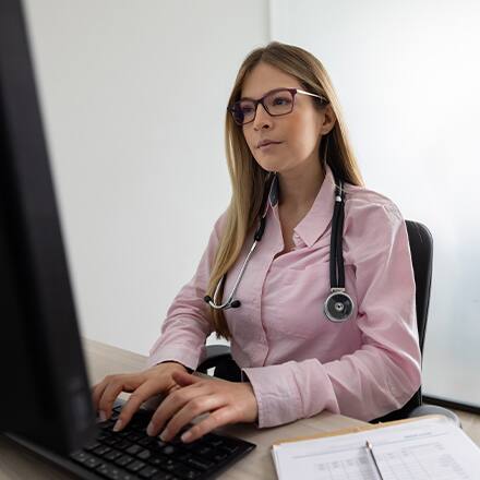A medical professional wearing a stethoscope and researching what healthcare administration is on her computer.