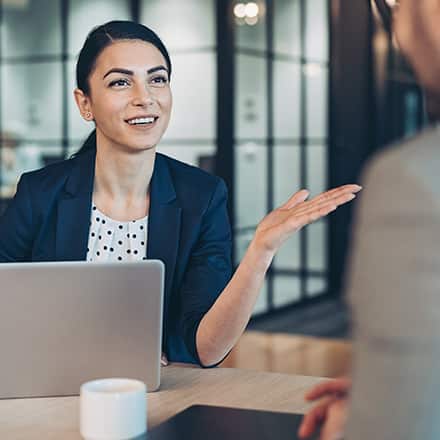A woman sitting behind a laptop speaking to a man about HR.
