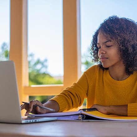  A student in a yellow sweater sitting at a desk working on her minor on her laptop