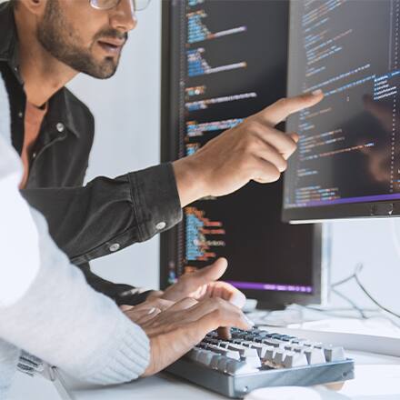 Two computer programmers using Python and reviewing code on a desktop computer.