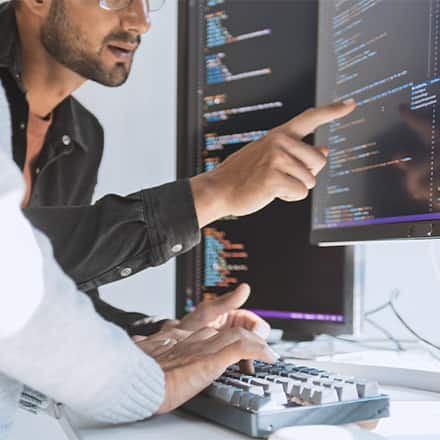Two computer programmers using Python and reviewing code on a desktop computer.