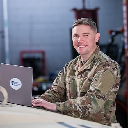 SNHU graduate and U.S. Army Reserve trainer coach Rob Thomas doing college coursework on a laptop.