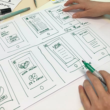 A web designer sketching out different design ideas with a green marker