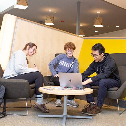 Three college students looking at a laptop while they study for a liberal arts degree.
