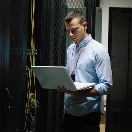 Man working as IT manager standing in a server room working on a laptop.
