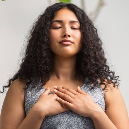 A woman meditating with her eyes closed and hands over her chest