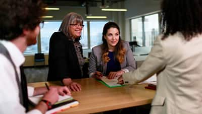 A team of three standing around a counter and looking at their leader as she points to a clipboard.