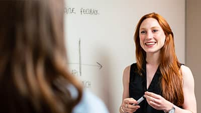 A leader at a whiteboard, listening to her employee.