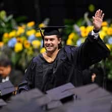 An SNHU graduate dressed in cap and gown, waving to his supporters.